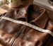 Tape measure laid across a folded brown leather jacket on a wooden table